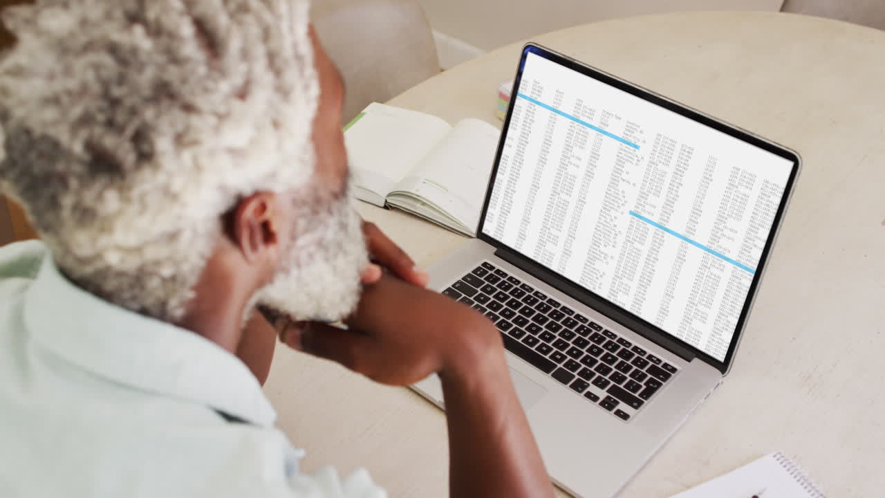 African american man sitting at desk watching coding data processing on laptop screen