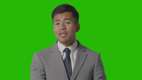 portrait of angry businessman in suit against green screen talking to camera