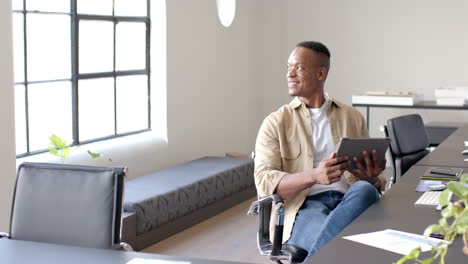 smiling businessman holding tablet and sitting in modern office workspace