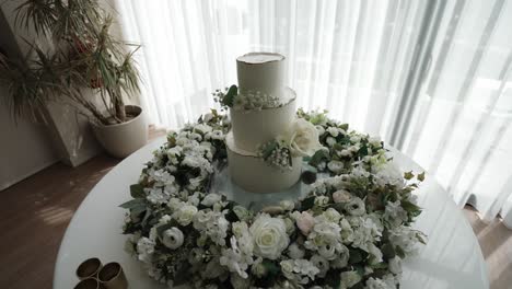elegant white wedding cake surrounded by soft floral wreath in bright natural light