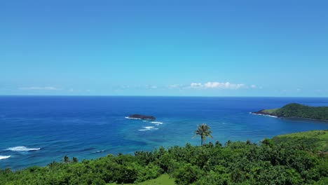 green mountainside to reveal tropical ocean breaks and blue sky, drone