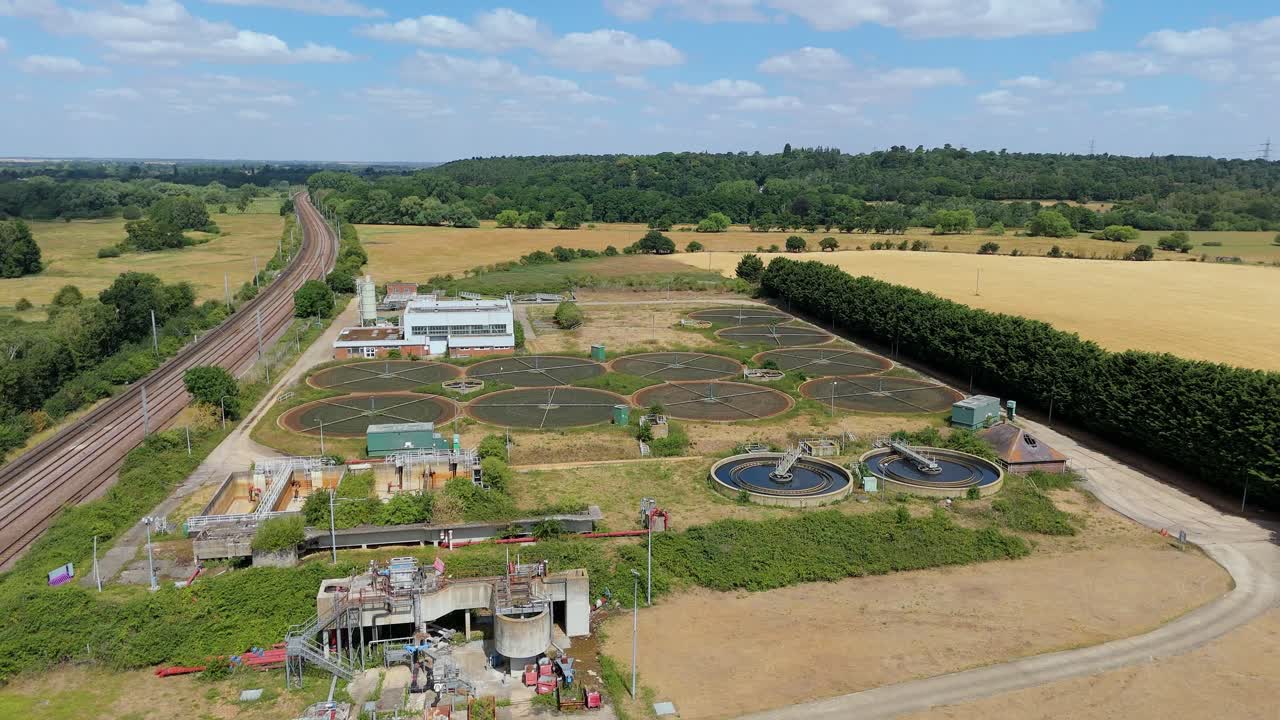 Cinematic aerial shot of Anglian water treatment plant filtration and settling pools next to train tracks UK
