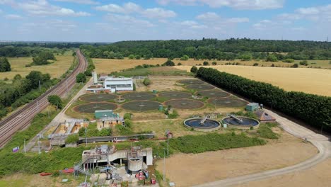 cinematic aerial shot of anglian water treatment plant filtration and settling pools next to train tracks uk