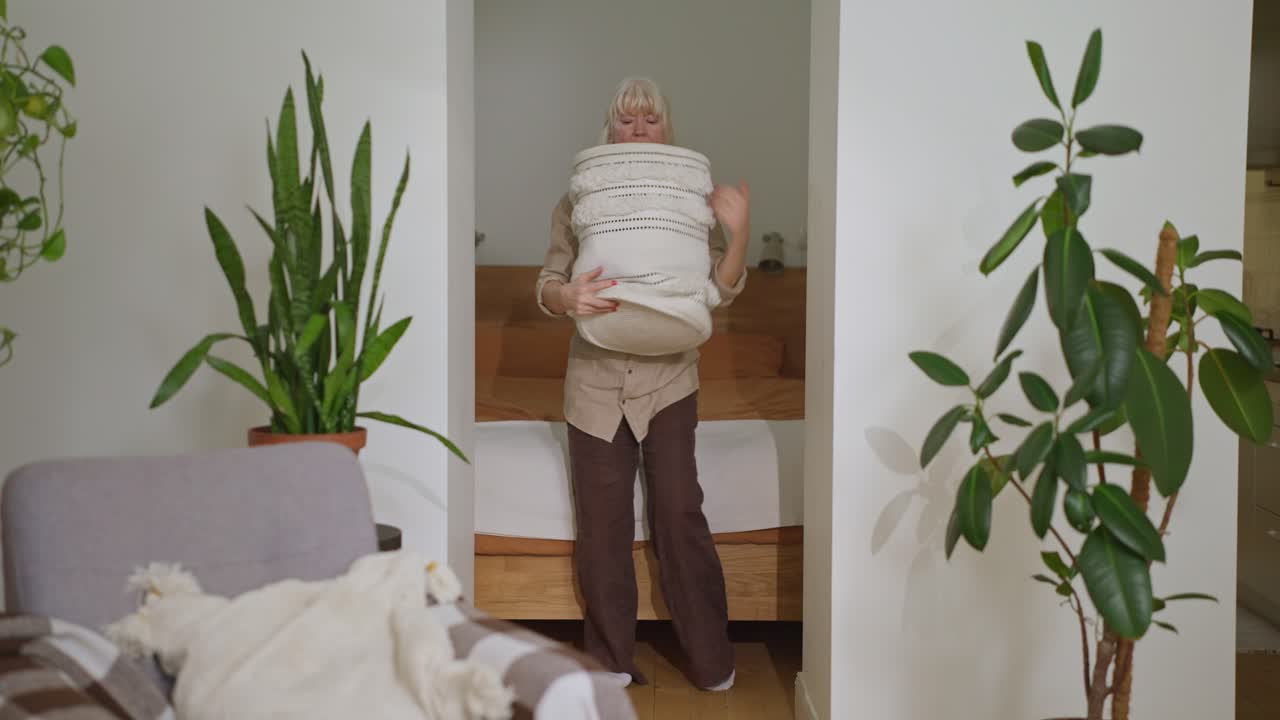 Elderly woman carrying a laundry basket in her bedroom