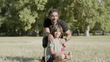 long shot of father with disability and son sitting on lawn