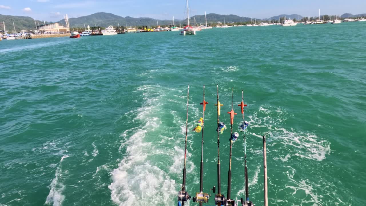 A catamaran navigates vibrant Phuket waters, showcasing fishing rods and scenic coastal views under bright sunlight