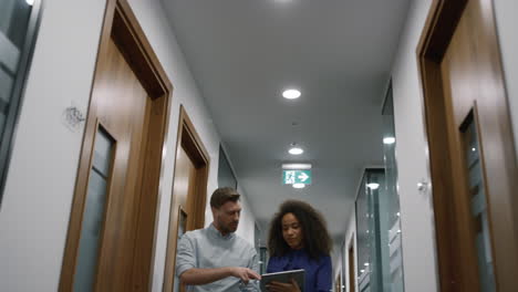 Multiracial business team talking finance plan using tablet in office hallway.