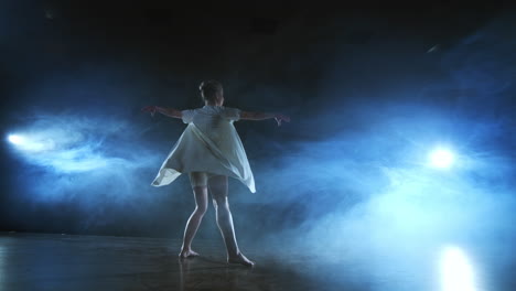 modern dance woman in a white dress dances a modern ballet jumps on the stage with smoke in the blue spotlights.