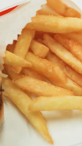 patatas fritas doradas y una hamburguesa en una bandeja negra con una mano alcanzando para elegir una. vista de cerca