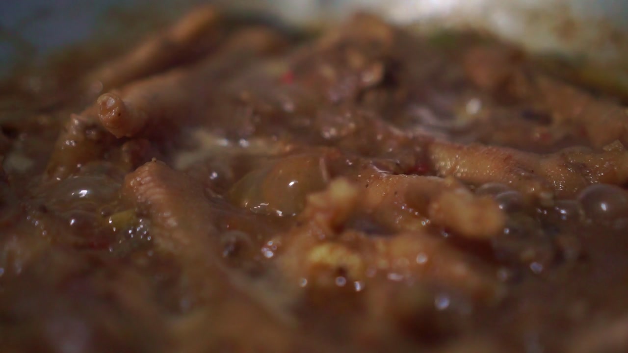 Chicken meat simmering in thick bubbling sauce. Macro cooking scene showing juicy chicken in rich gravy.