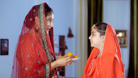 a pretty indian lady feeding indian sweet / laddu to her daughter - family bonding, a festive season, a tasty sweet, festival celebrations