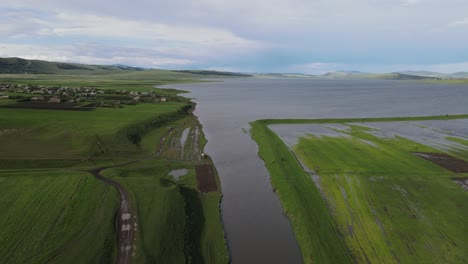 Aerial-shot-of-a-lake-surrounded-by-meadows-villages-villages-old-houses-mountains