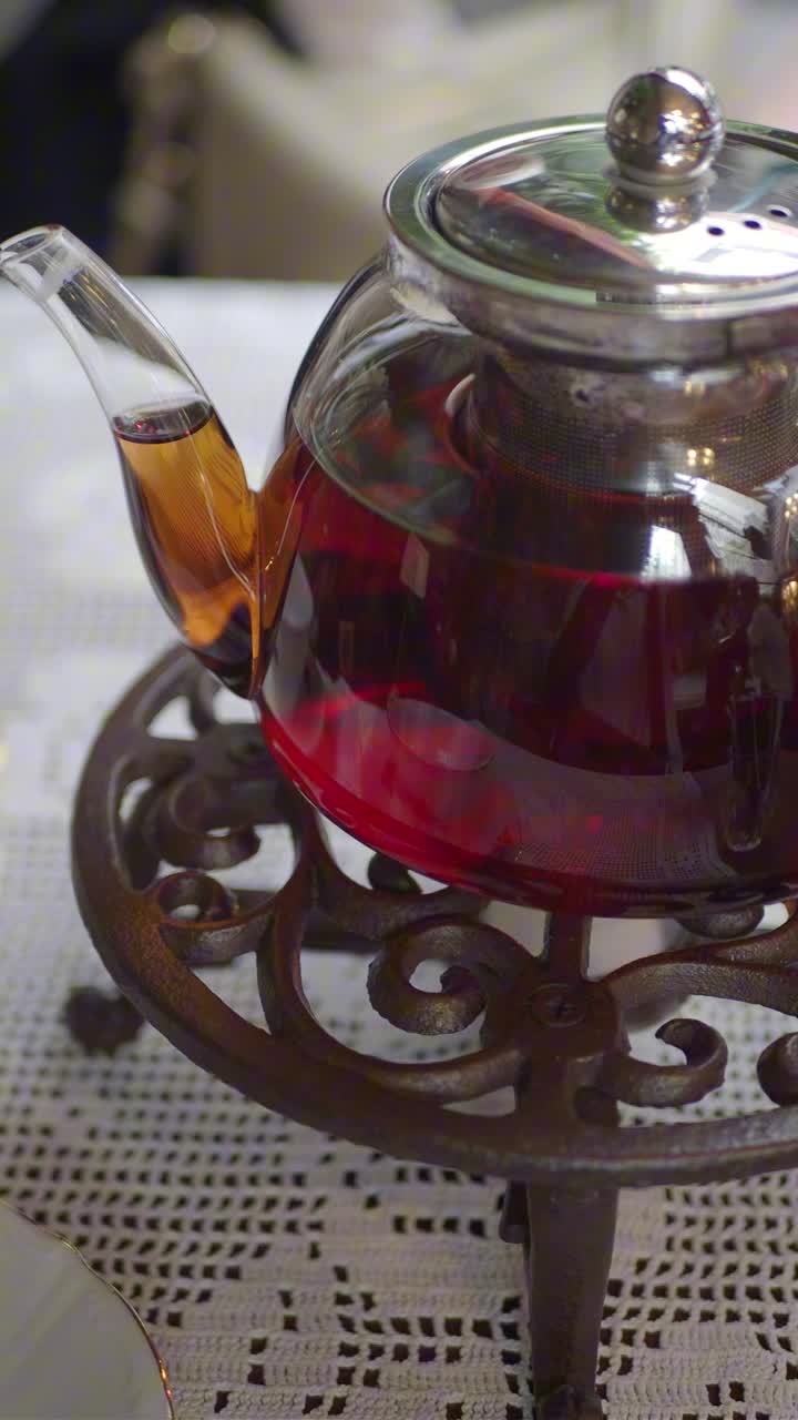 Tisana rossa in infusione in una teiera di vetro su uno scalda-tè.