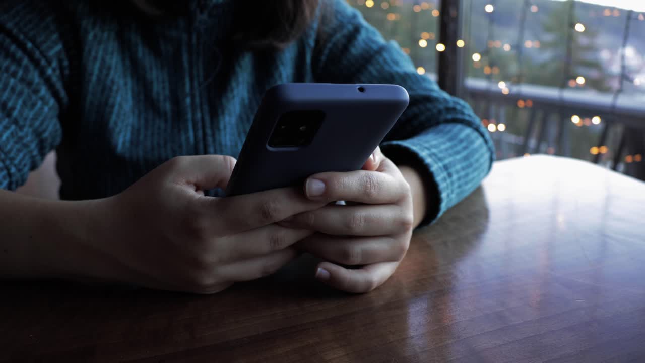 niña sosteniendo su teléfono y desplazándose por las redes sociales, primer plano de sus manos y teléfono mientras descansan en una mesa de café