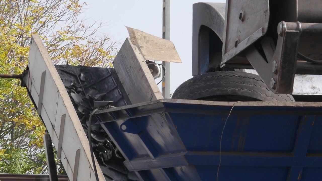 Macchina industriale pesante per il riciclaggio che alimenta pneumatici usati in una tramoggia di triturazione, con un nastro trasportatore che sposta i pezzi di gomma.