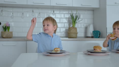 A-young-beautiful-mother-in-a-white-dress-with-two-children-is-smiling-and-eating-fresh-burgers-in-her-kitchen.-Happy-family-homemade-food-healthy-foods