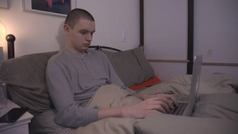 young man working and using a laptop computer on his bed at night