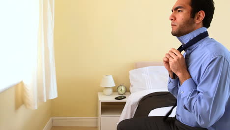 Businessman-tying-his-tie-sat-on-bed