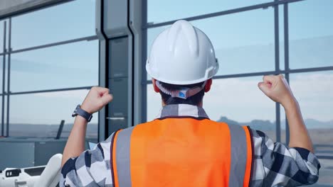vista cercana de atrás de un ingeniero asiático con casco de seguridad de pie levantando las manos celebrando trabajando en una fábrica de alta tecnología, analizando el concepto de máquina robótica