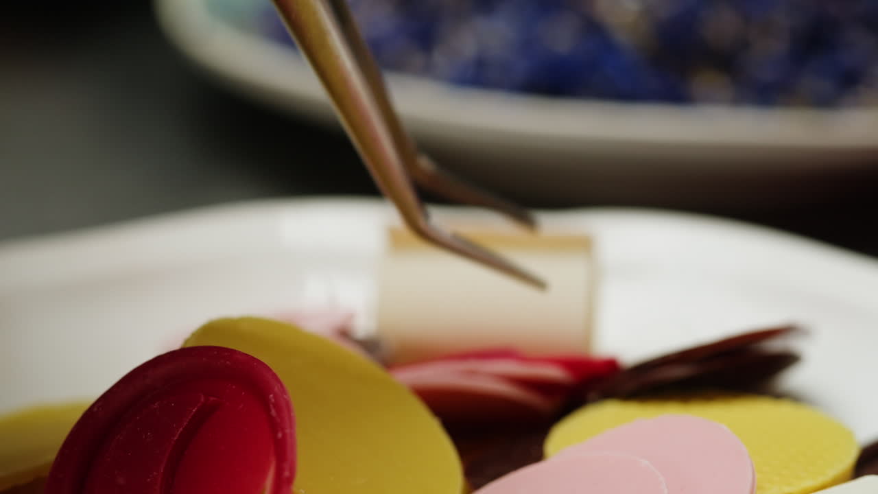 Close up of a plated dessert, featuring colorful chocolate components being arranged.