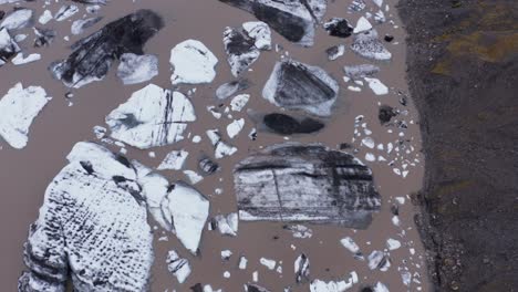 large calved iceberg pieces floating in brown glacial lagoon water, top down