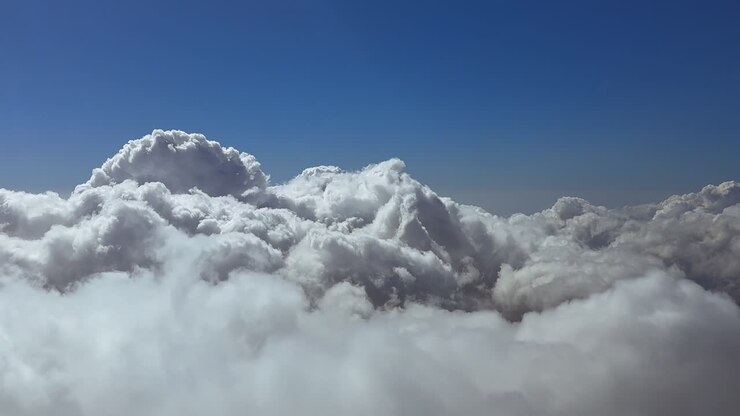 immersive cockpit view while flying peacefully over an endless layer of storm clouds under a high-altitude intense blue sky. Footage taken from a jet cockpit
