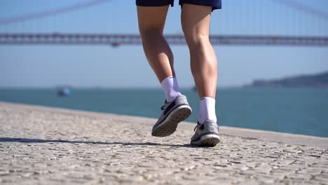 legs of young sportsman running on pavement at riverside