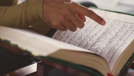 primer plano de una copia abierta del corán en un stand en casa con un hombre recitando o leyendo