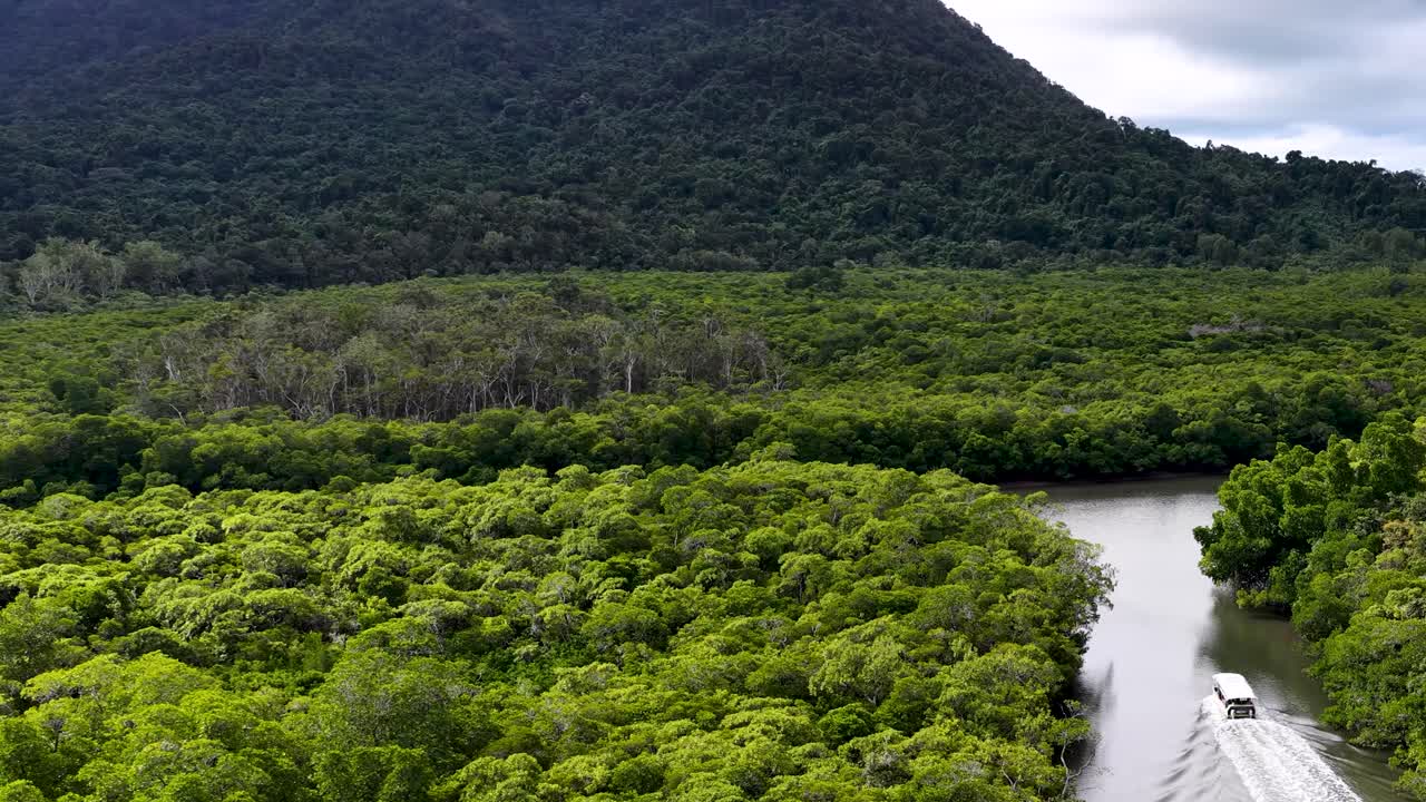 Aerial view of motorboat traveling on winding river through dense rainforest under overcast daylight