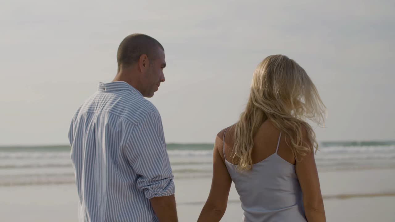 Back medium shot of happy couple walking along seashore.