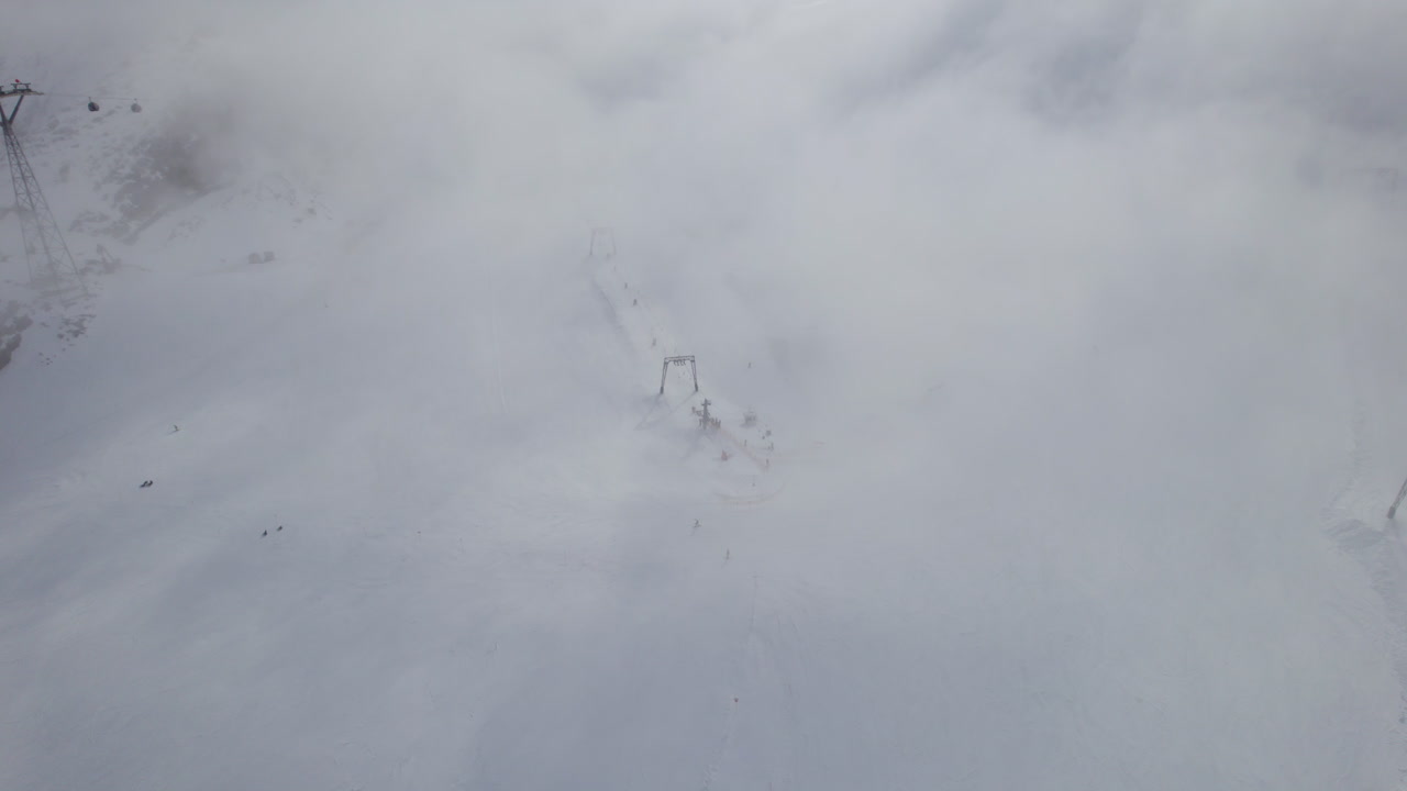 흐리고 안개가 자욱한 날에 스키어가 눈 덮인 산을 타는 공중 하향식 스키장