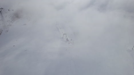 área de esquí aérea de arriba hacia abajo con esquiador esquiando montaña nevada durante el día nublado y brumoso