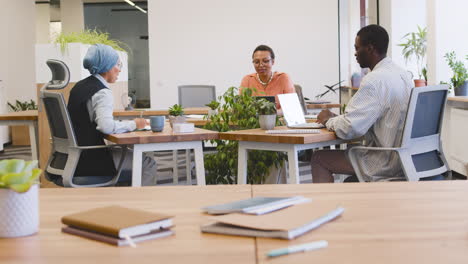 muslim businesswoman, businesswoman and young worker are working sitting on their desk while talking to each others in the office