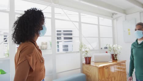 office colleagues wearing face masks greeting each other by touching elbows at office