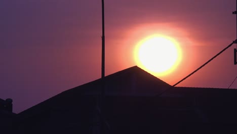 time lapse of a circular ball sun setting behind a silhouette of a roof top of a building