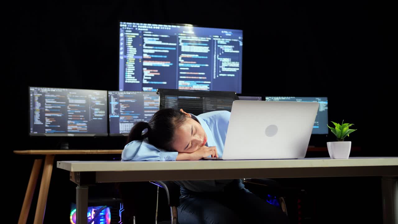 Asian Female Programmer Sleeping While Writing Code By A Laptop Using Multiple Monitors Showing Database On Terminal Window Desktops In The Office