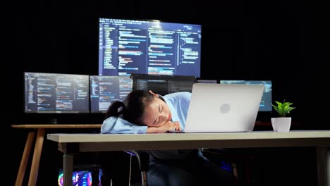 programadora asiática durmiendo mientras escribe código en una computadora portátil usando múltiples monitores que muestran la base de datos en los escritorios de ventana de terminal en la oficina