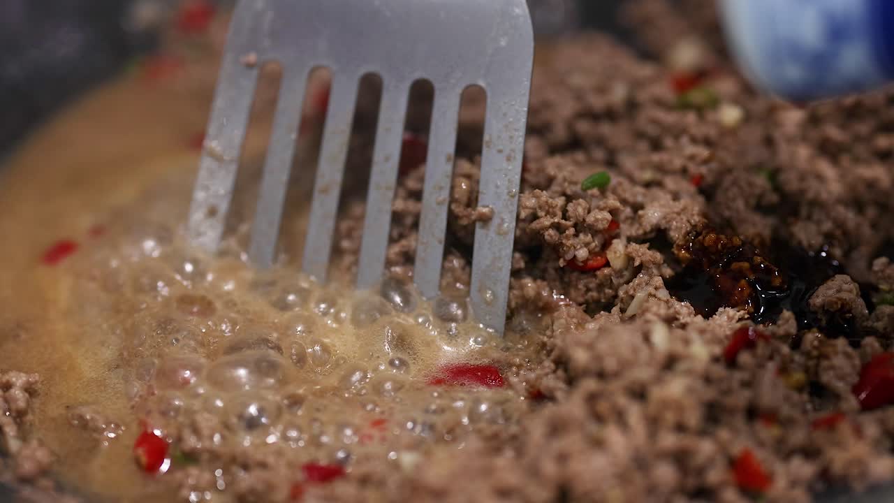 Close-up of beef stir fry preparation with spatula in a bubbling sauce. Warm lighting enhances the cooking process