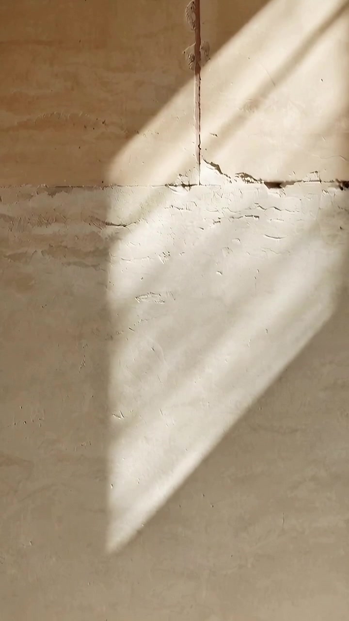 Vertical video: Shifting sunlight patch moving down plaster wall in bare room, triggered by window