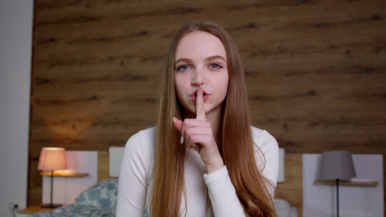 Mujer joven pidiendo silencio con el dedo en los labios, para no contar el secreto, haciendo el gesto de cerrar la boca con una cremallera
