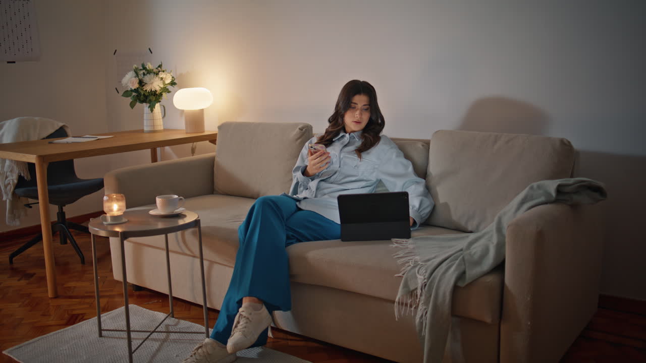 mujer relajada navegando por el teléfono inteligente en el interior del sofá de la noche. mujer buscando tableta