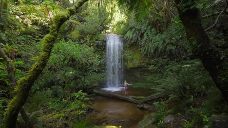 female hiker standing on fallen tree at secluded koropuku falls in new zealand