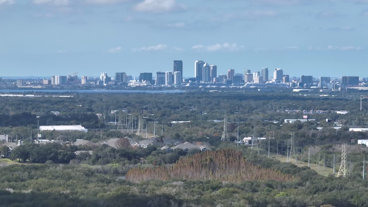 Vista aerea dello skyline di Tampa da Brandon, Florida, con moderni grattacieli che si ergono oltre i verdi paesaggi suburbani sotto un cielo azzurro limpido. Contrasto tra città e natura. Campo largo