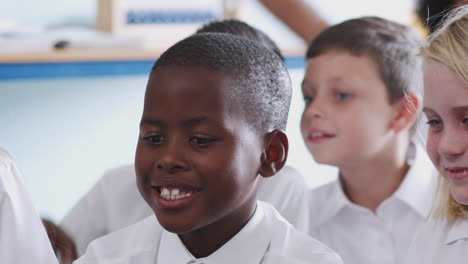 group of elementary pupils wearing uniform sitting on floor raise hands to answer question in class