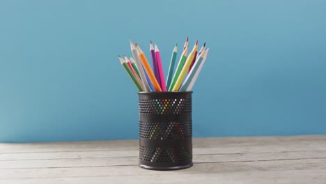 video of cup with crayons in wooden table over blue background