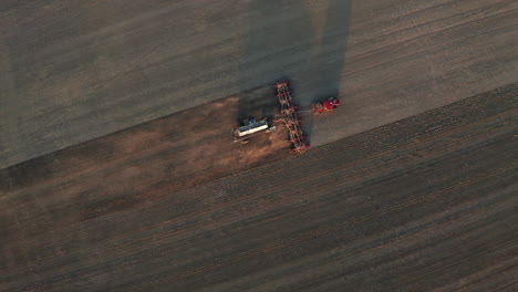 Impresionante-Vista-De-La-Máquina-Tractora-Agrícola-De-Siembra-Que-Viaja-Sobre-Tierra-Plana-Y-Filas-De-Tierras-De-Cultivo-Polvorientas-Al-Atardecer,-Saskatchewan,-Canadá,-Directamente-Sobre-La-Estática-Aérea