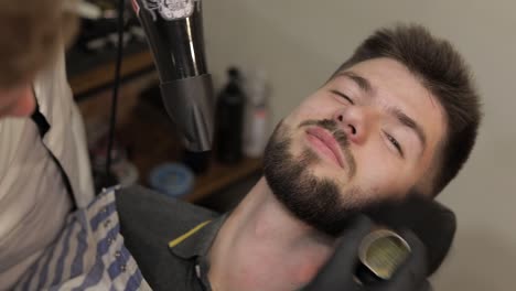 Client-with-black-beard-during-beard-shaving-in-barber-shop.-Groom,-masculine