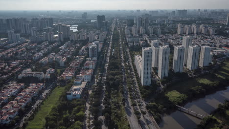 Drone-hyperlapse-along-highway,-ultra-modern-city-with-river,-green-space-and-high-rise-buildings-seen-from-the-air-on-a-sunny-day