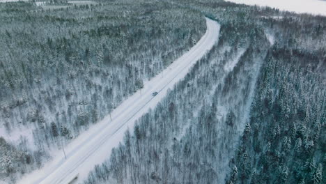 Vista-Aérea-Del-Vehículo-Que-Conduce-A-Través-De-Caminos-Nevados-En-Laponia,-Finlandia---Disparo-De-Drones