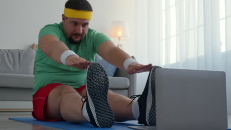 man stretching at home while following an online workout session